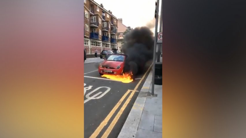 Bystanders attempt to stop a burning car rolling along a busy London street