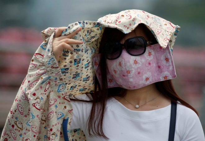 A woman wearing a face mask shields her face from the sun as haze shrouds Singapore