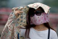 A woman wearing a face mask shields her face from the sun as haze shrouds Singapore