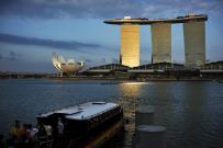 Visitors board a traditional bumboat vessel as sunlight shines on the Marina Bay Sands integrated resort during dusk in downtown Singapore