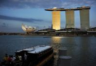Visitors board a traditional bumboat vessel as sunlight shines on the Marina Bay Sands integrated resort during dusk in downtown Singapore