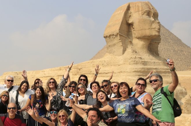 Tourists smile and cheer as they take a souvenir photo in front of the Sphinx at the Giza Pyramids