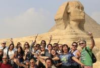 Tourists smile and cheer as they take a souvenir photo in front of the Sphinx at the Giza Pyramids