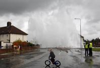 A boy cycles through a puddle as a burst main shoots a plume of water into the air in the Huyton area of Liverpool, northern England, July 18, 2011. The burst main led to localized flooding and evacuations of residents. REUTERS/Phil Noble (BRITAIN - Tags: