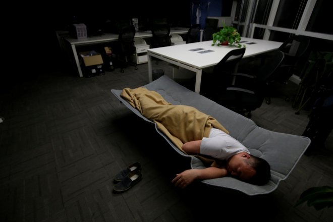 Ma Zhenguo, a system engineer at RenRen Credit Management Co., sleeps on a camp bed at the office after finishing work early morning, in Beijing, China, April 27, 2016. Office workers sleeping on the job is a common sight in China, where a surplus of chea