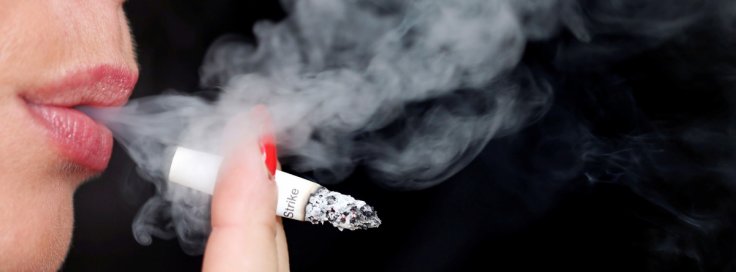 Smoke rises from a burning cigarette as a woman smokes on the street in Bordeaux