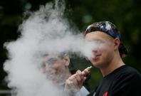 Man exhales e-cigarette vapour in park in Kiev