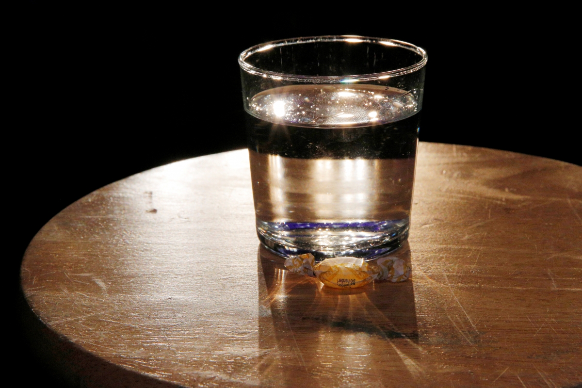 A cough drop and a glass of water are placed on a stool