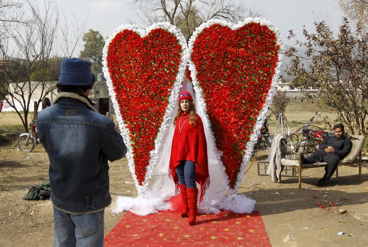 An Afghan man takes a picture of his sister in front of large heart shaped flower arrangement at a flower