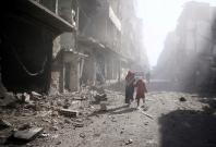 People walk past a damaged site after an airstrike in the besieged rebel-held town of Douma, eastern Ghouta in Damascus, Syria