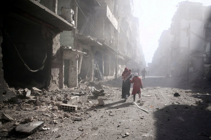 People walk past a damaged site after an airstrike in the besieged rebel-held town of Douma, eastern Ghouta in Damascus, Syria