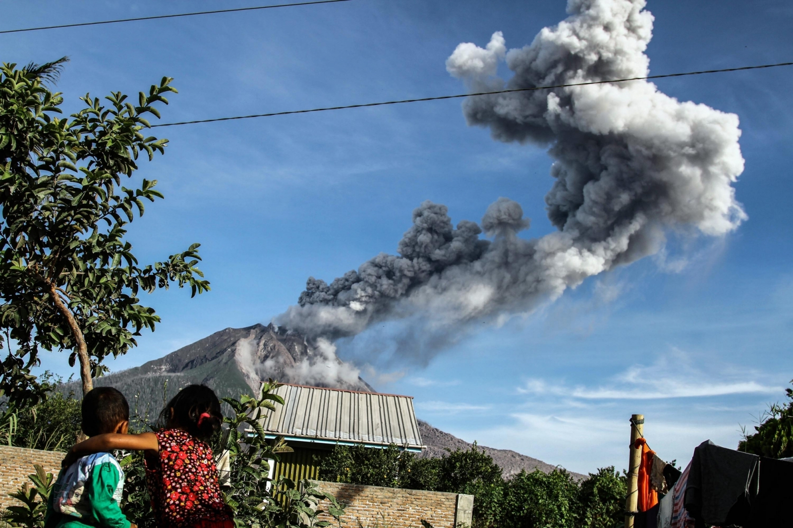 Children watch as Mount Sinabung volcano spews smoke and ash in Karo, North Sumatra of Indonesia