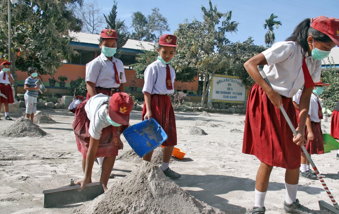 Students clean their school yard from ash after Mount Sinabung volcano erupted on Monday at Payung village in Karo