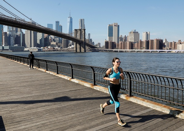 A woman runs along the East River through Brooklyn Bridge Park during unseasonably warm weather in Brooklyn, New York