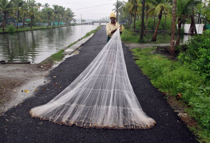 A fisherman arranges his fishing net along a road as it drizzles on the outskirts of the southern Indian city of Kochi