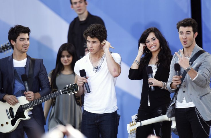 Jonas Brothers (L-R) Joe, Nick, and Kevin smile onstage with Demi Lovato