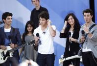 Jonas Brothers (L-R) Joe, Nick, and Kevin smile onstage with Demi Lovato