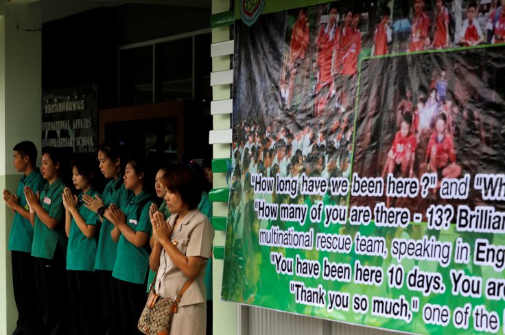 Schoolmates pray next to a banner showing 12 missing schoolboys, who were trapped inside a flooded cave, at Mae Sai Prasitsart school, in the northern province of Chiang Rai, Thailand, July 9, 2018.